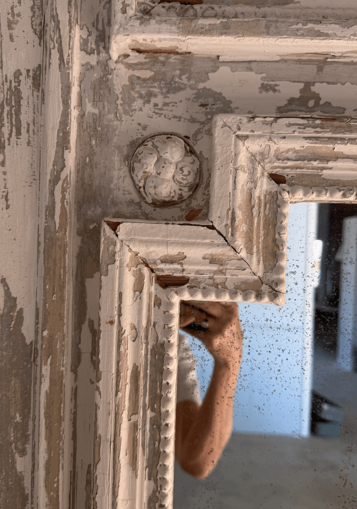 Close-up of a carved corner rosette on the frame, showing deeply chipped and flaking layers of old paint over wood