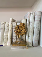 Row of antique French ledger print book covers with handwritten script standing upright on a shelf, with a small gilt metal flower spray on a crystal cluster base placed among them.