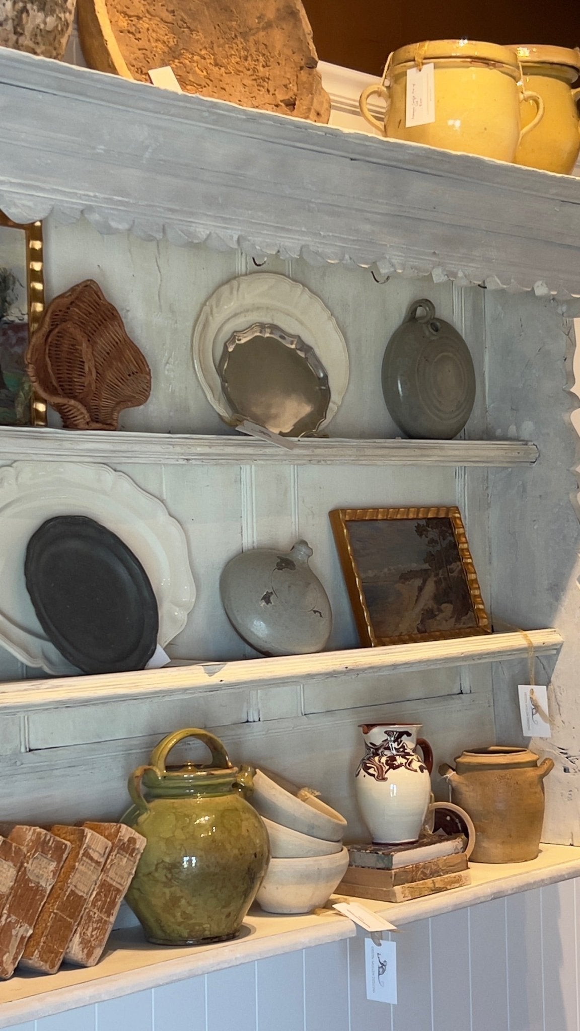 The green glazed jug displayed on a painted hutch shelf among stacked bowls, plates, framed art, and other ceramics