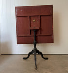 Table shown tilted, with the red-painted underside of the top visible above the black tripod base