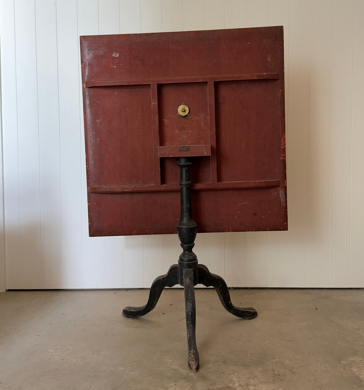 Table shown tilted, with the red-painted underside of the top visible above the black tripod base