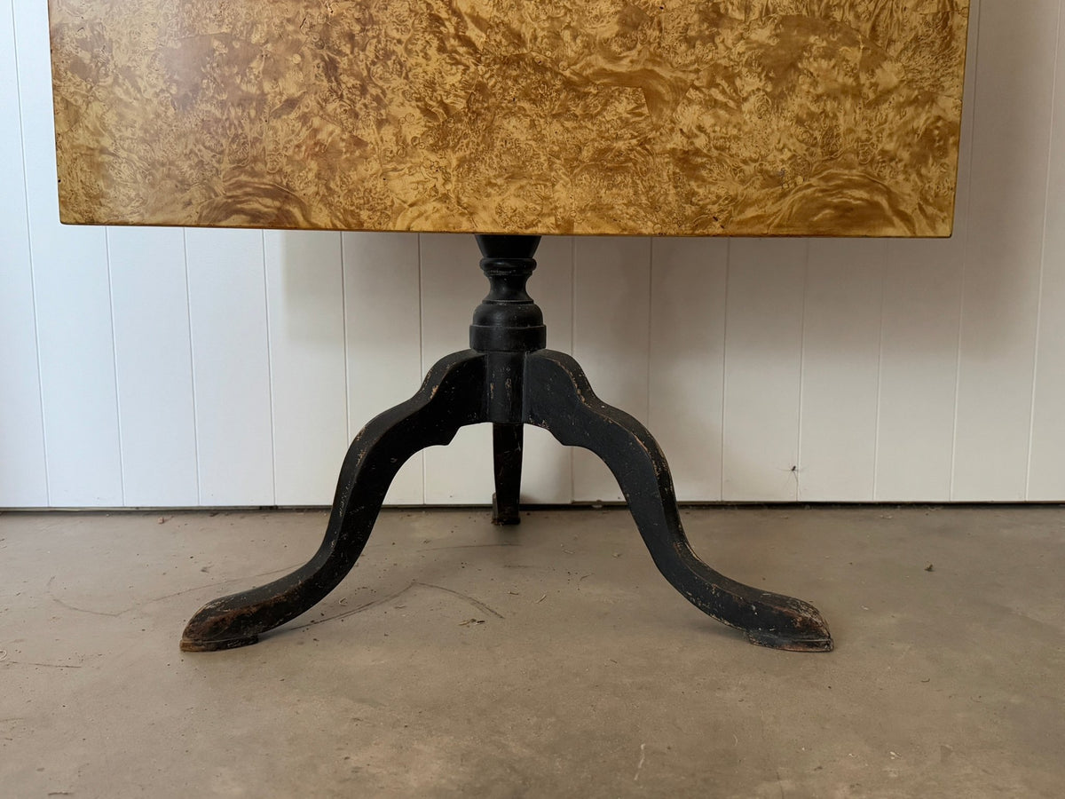 Close-up of the black cabriole tripod base beneath the burl wood tabletop