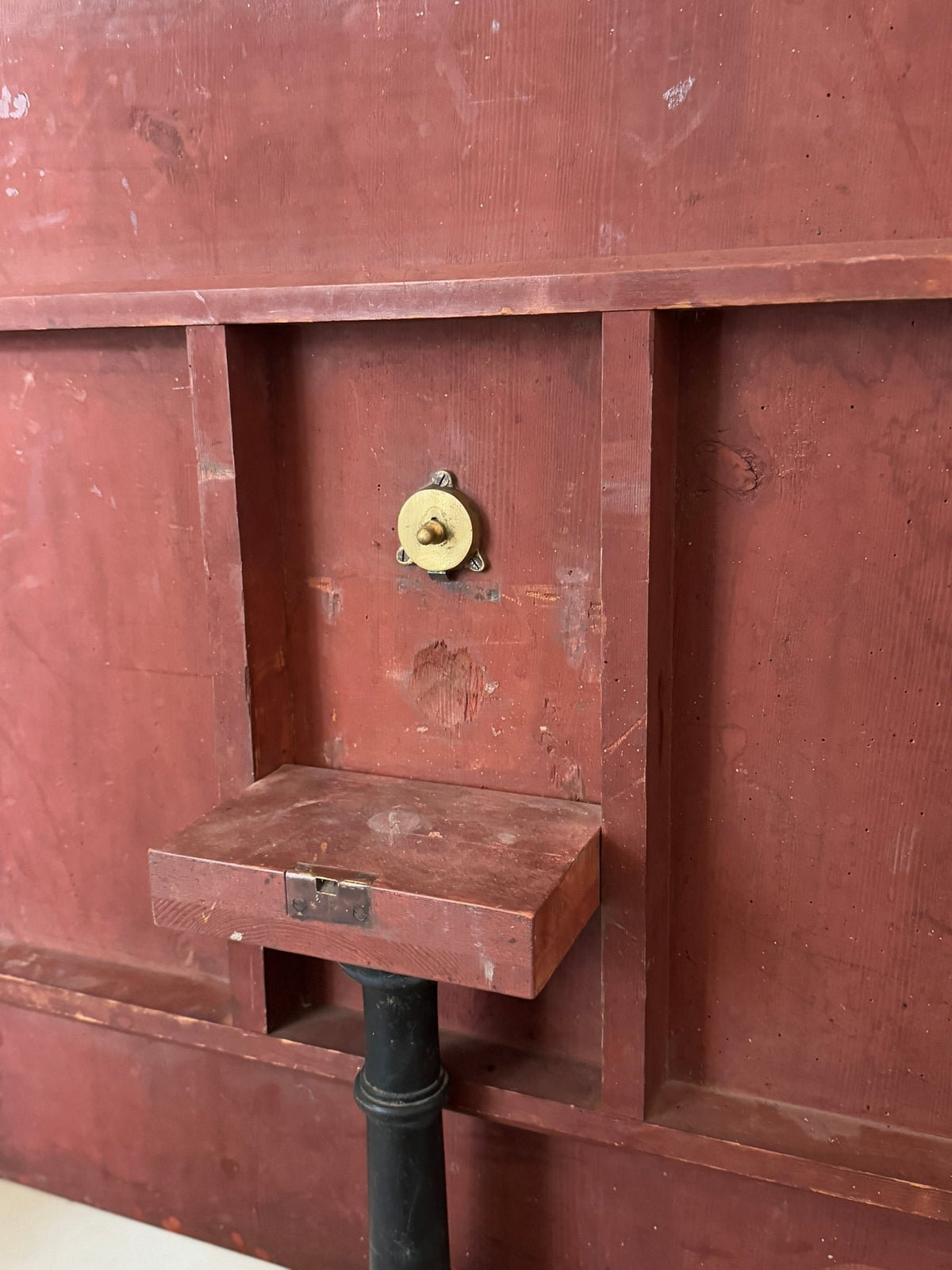 Underside of the tilt-top table showing the red-painted wood frame and brass tilt latch