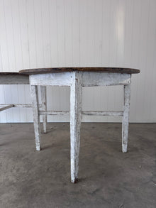 Close-up of one demilune's tapered legs and apron, showing distressed white paint with rusted nail heads at the joints