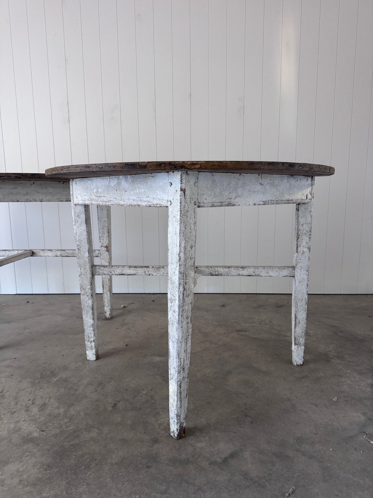 Close-up of one demilune's tapered legs and apron, showing distressed white paint with rusted nail heads at the joints