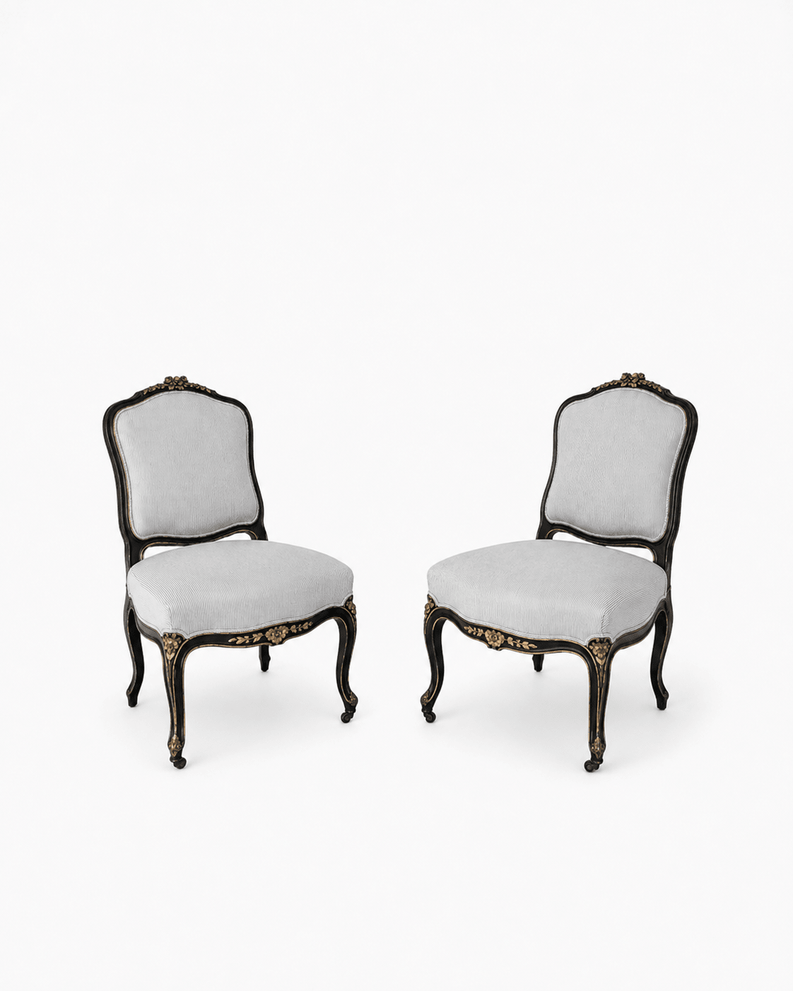 Pair of ebonized Louis XV-style side chairs with gilt floral accents, cabriole legs, and gray striped upholstery, shown on a white background