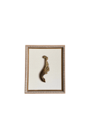 Small carved gilt wood fragment shaped like a scrolling acanthus leaf, mounted on a linen mat in a patterned paper frame.