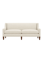 Quick Ship Kenilworth sofa with slope arms, two seat cushions, and tapered wood legs, upholstered in cream fabric, against a white background.