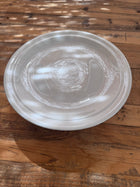 Overhead close-up of a white ironstone cakestand's plate surface, showing subtle glaze rings and crazing in dappled light