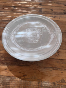 Overhead close-up of a white ironstone cakestand's plate surface, showing subtle glaze rings and crazing in dappled light